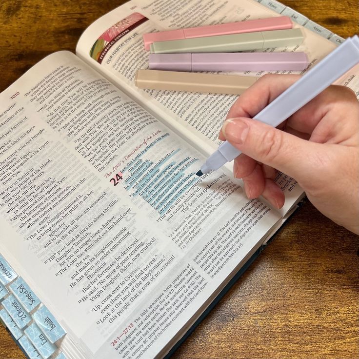 a person is holding a pen over an open book on a wooden table with keyboard keys