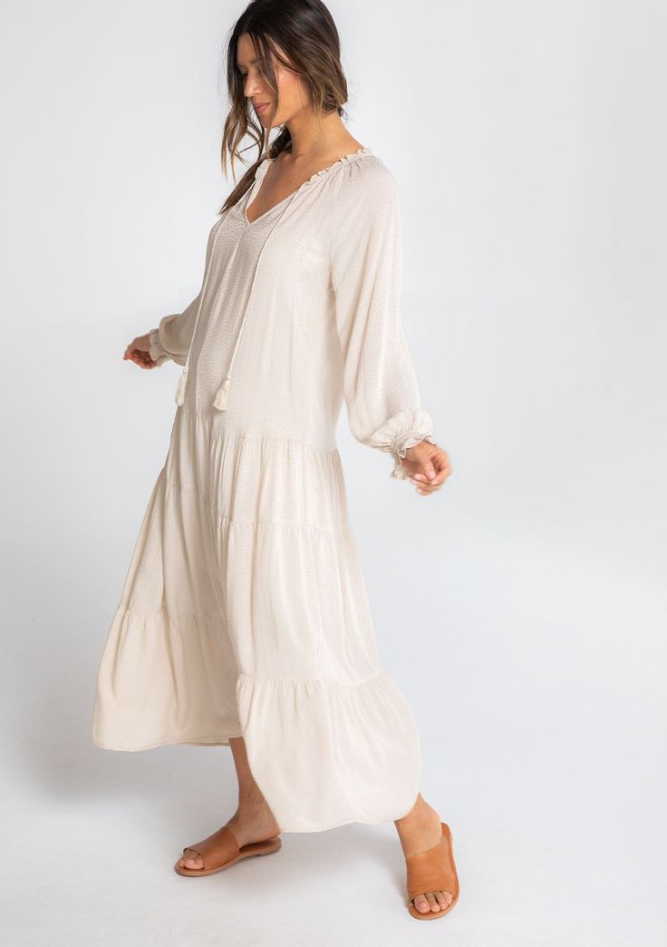 We all need that one dress that can check multiple boxes. This versatile bohemian style features a classic peasant dress silhouette, a relaxed fit, and delicate textured dot details throughout. Pair it with flat sandals for beach days, ankle boots, and a hat for date nights, or with statement heels for dinner parties. Featuring a flattering dropped waist, a flirty tiered skirt, and a pretty split v-neckline with tassel ties. Jacquard dot Relaxed fit Long raglan sleeves Ruffled wrist cuff Maxi le Bohemian Long Sleeve Tiered Summer Dress, Flowy V-neck Peasant Boho Dress, Bohemian Tiered Maxi Dress For Daywear, Bohemian Peasant Dress Midi Length For Daywear, Bohemian Midi-length Peasant Dress For Daywear, Bohemian Midi Length Flowy Peasant Dress, Flowy Bohemian Peasant Dress For Daywear, Flowing Peasant Maxi Dress For Spring, Bohemian Tiered Dress For Vacation