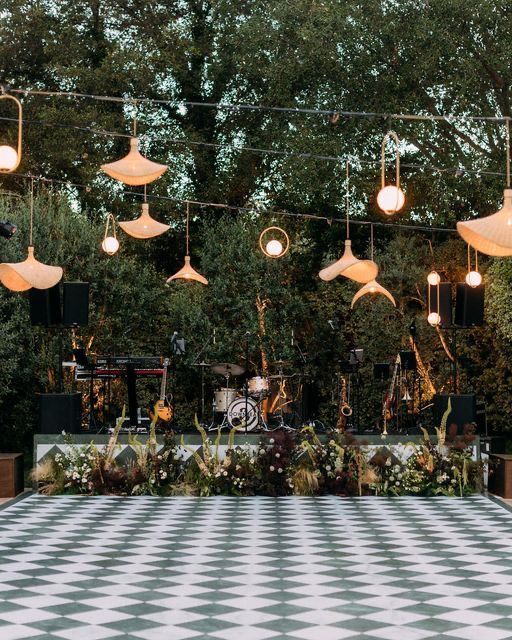 an outdoor stage with lights and plants hanging from it's sides, surrounded by greenery