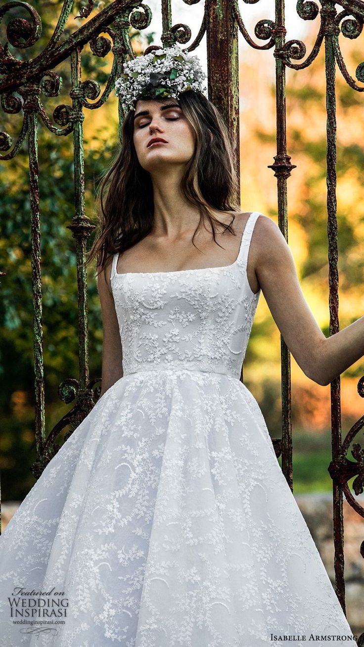 a woman wearing a white dress standing in front of an iron gate with a wreath on her head