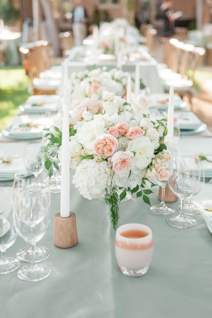 a table set with white and pink flowers, candles and wine glasses for an elegant centerpiece