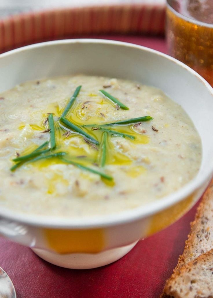 a white bowl filled with soup next to a slice of bread on a red place mat