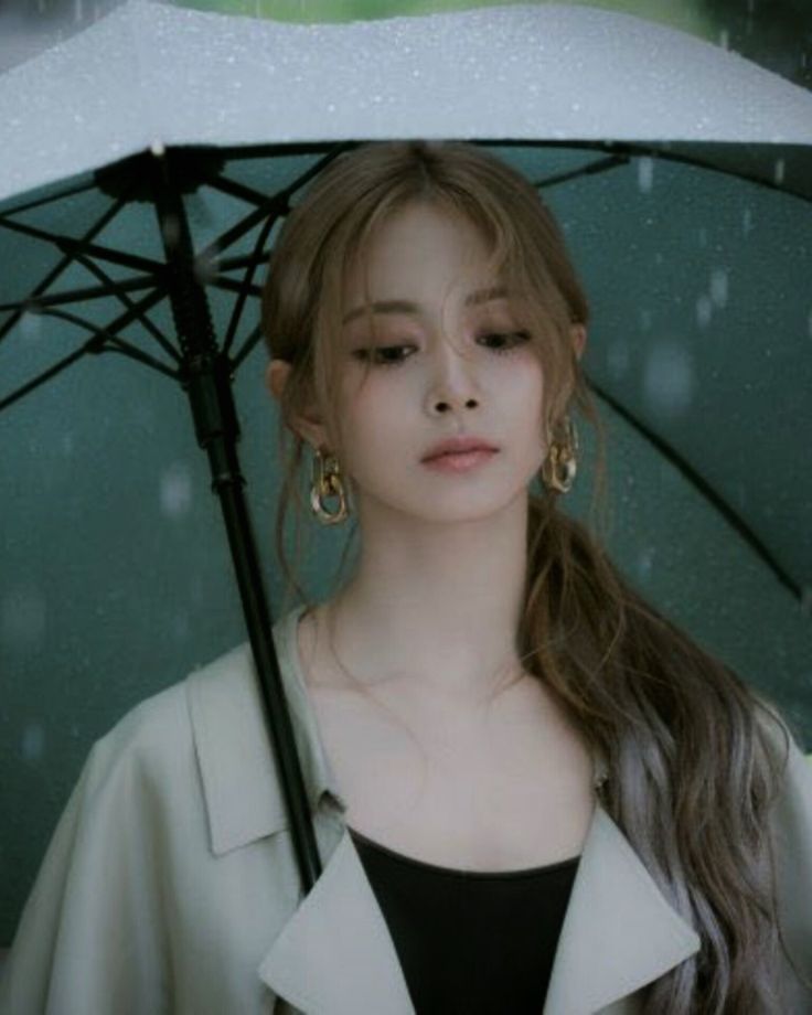 a woman with long hair holding an umbrella in the rain while wearing earrings