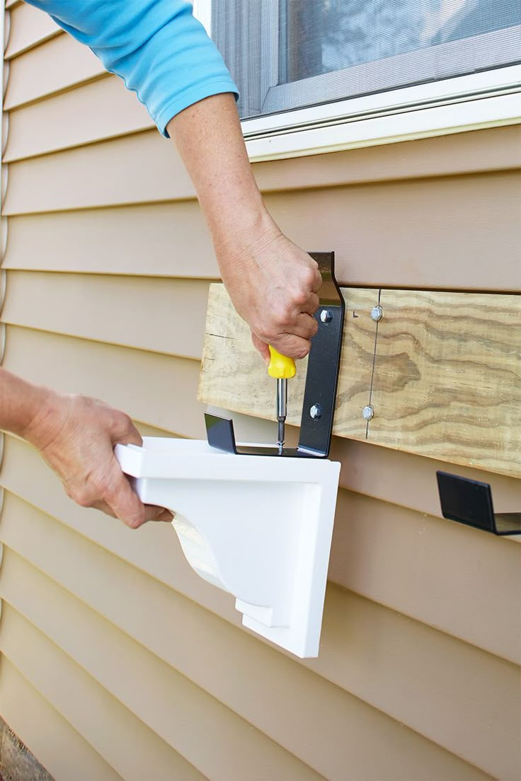 a person using a pair of scissors to attach a piece of wood on the side of a house