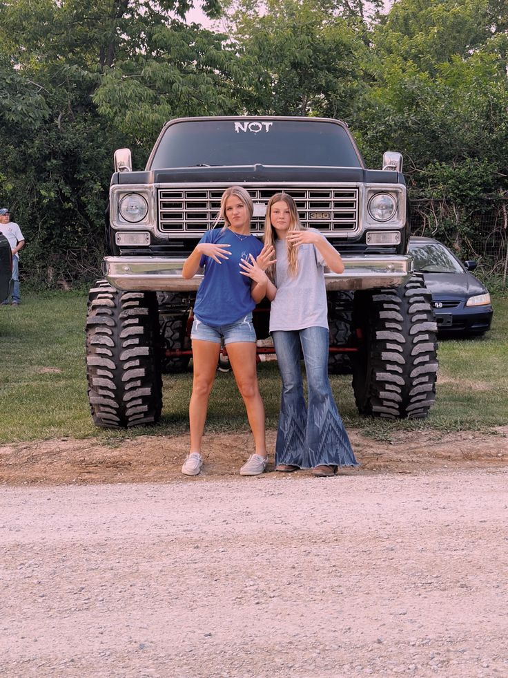 two women standing in front of a monster truck with their arms around each other's shoulders