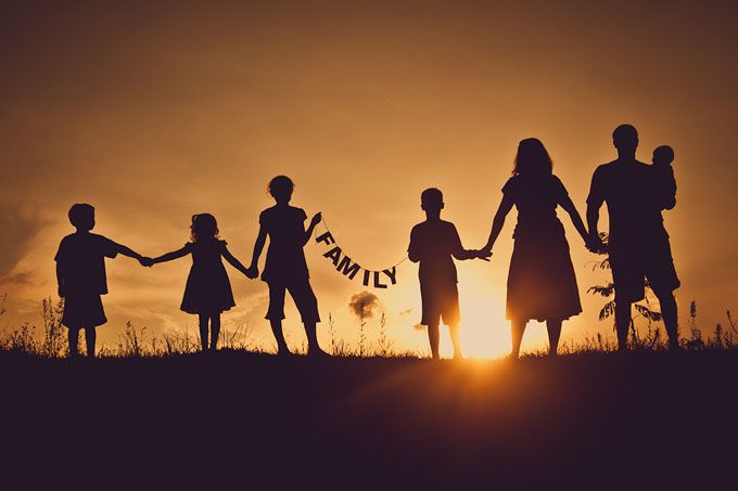 silhouettes of people holding hands with the sun setting in the sky behind them,