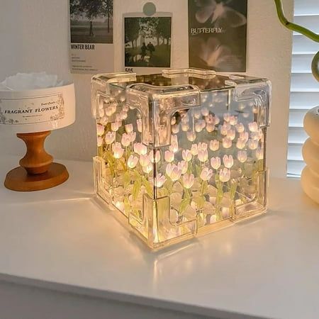 a clear box with flowers in it sitting on a table next to a lamp and other items