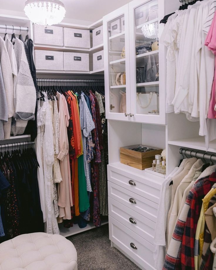 an organized closet with white drawers and clothes hanging on the racks, including shirts and pants