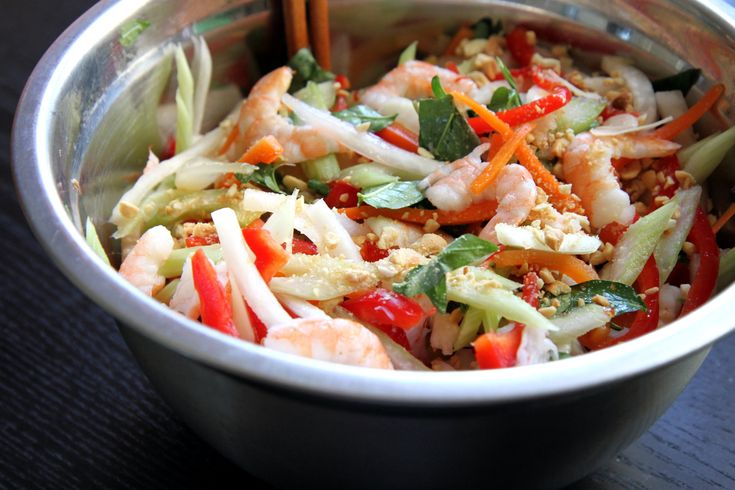 a bowl filled with shrimp, carrots and lettuce next to chopsticks