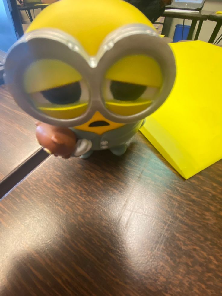 a yellow and gray toy with big eyes sitting on top of a wooden table