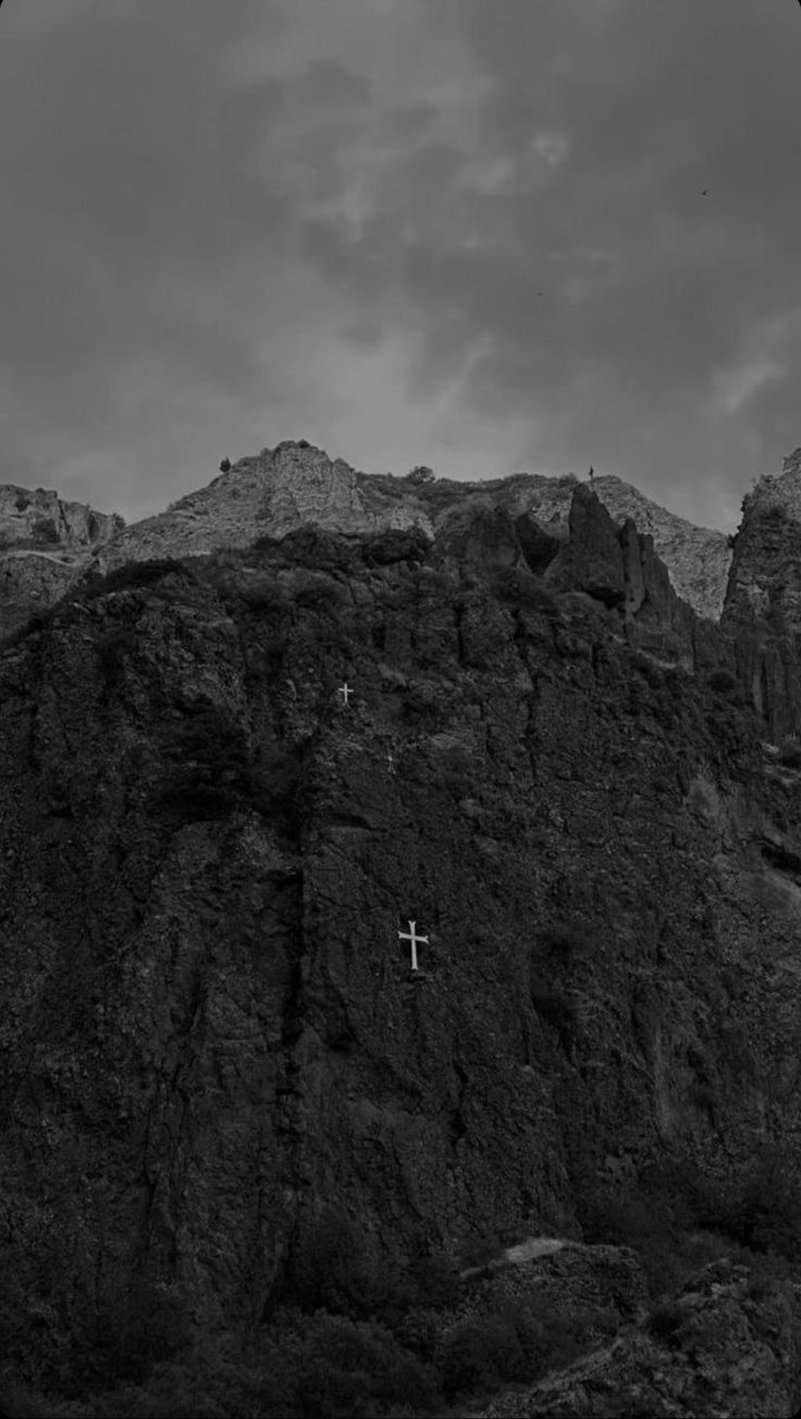 a cross on the side of a mountain under a cloudy sky