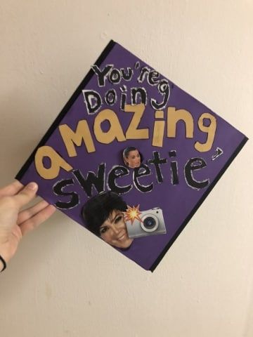 a hand holding up a purple graduation cap with the words you're doing amazing sweetie on it