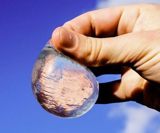 a hand holding a small glass ball in front of a blue sky with white clouds