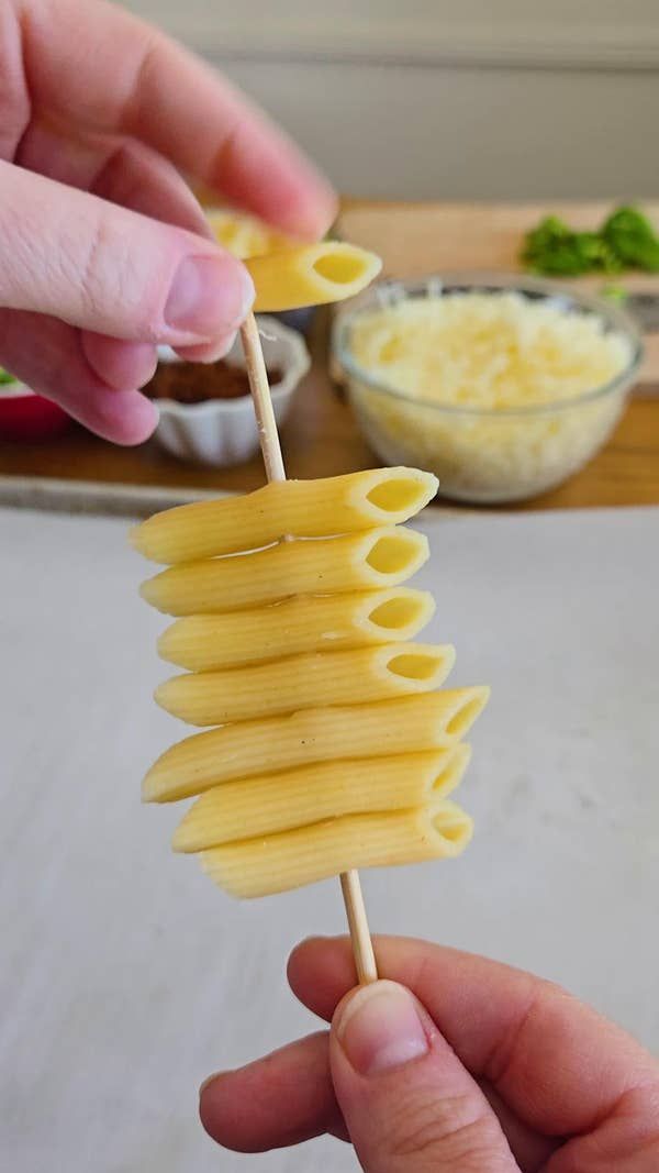 a person holding a toothpick with pasta on it in front of some other food