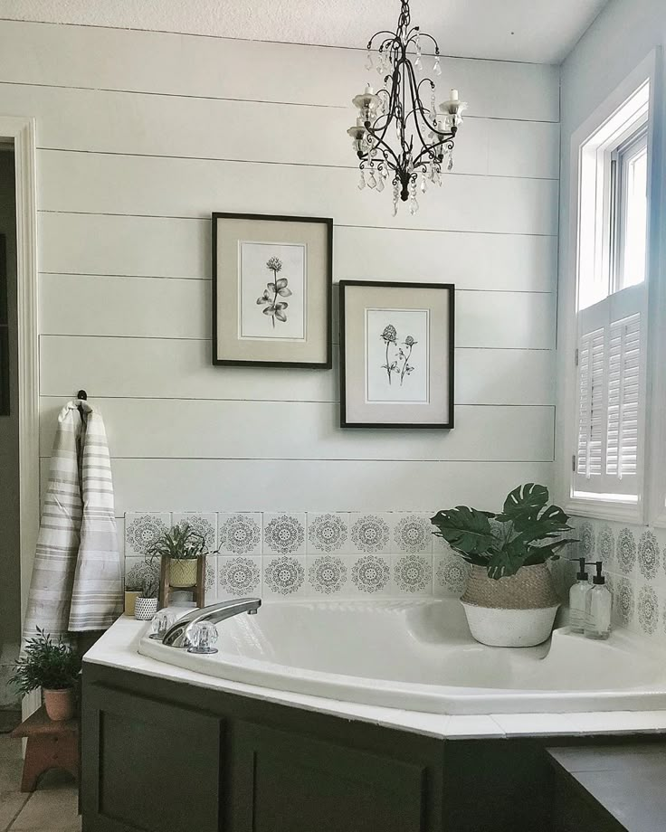 a bath tub sitting under a chandelier next to two pictures on the wall