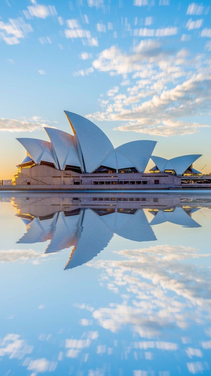 the sydney opera house in australia is reflected in the water at sunset with clouds and blue sky