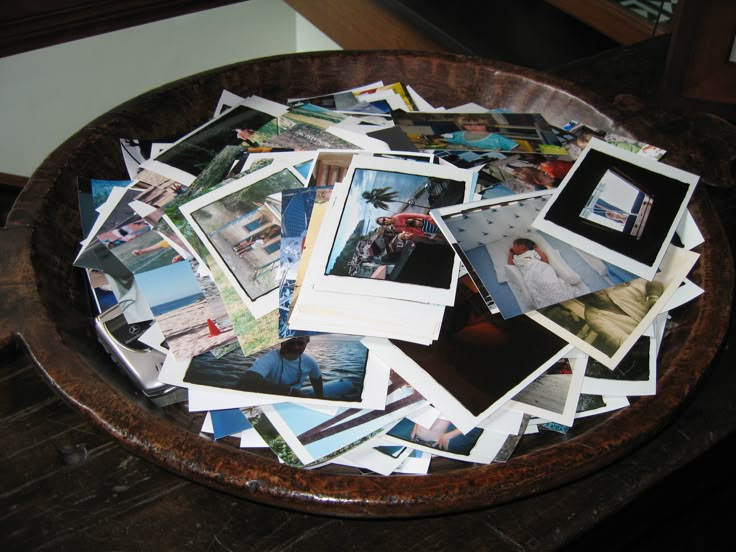 a wooden bowl filled with lots of pictures on top of a table next to a wall