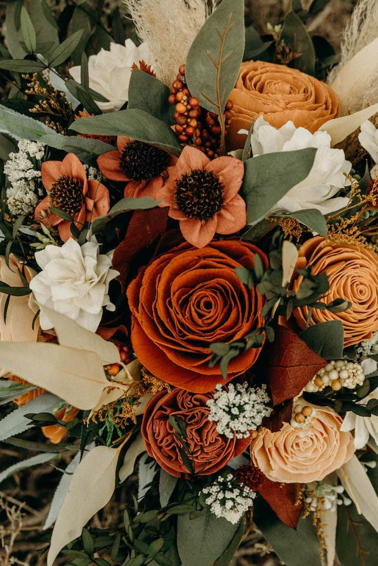 an arrangement of flowers and greenery is arranged in a bouquet on the ground with dry grass