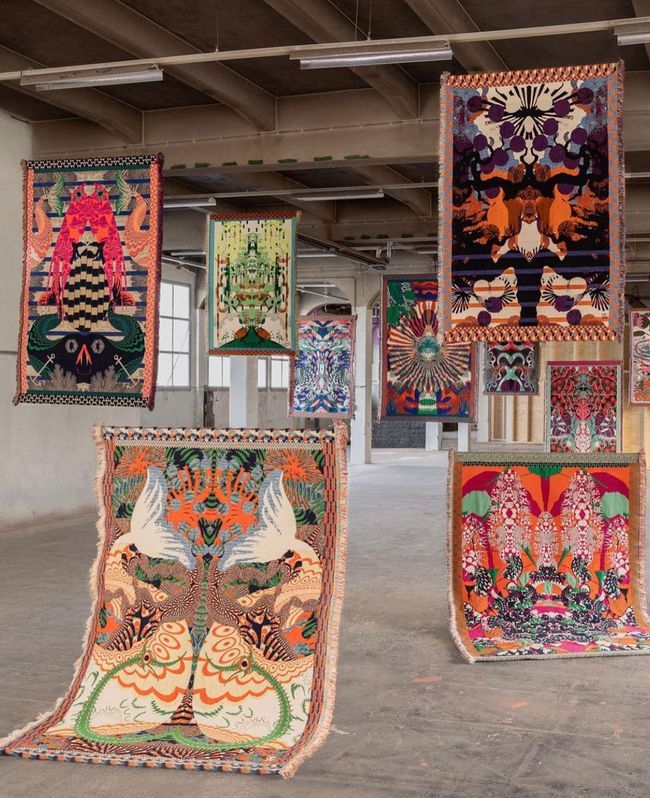 several colorful rugs hanging from the ceiling in an empty room with concrete flooring