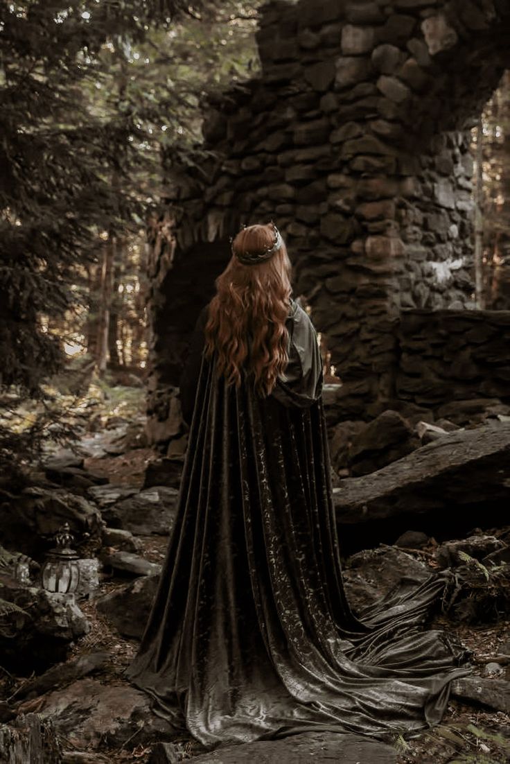 a woman with red hair wearing a black cloak in the woods