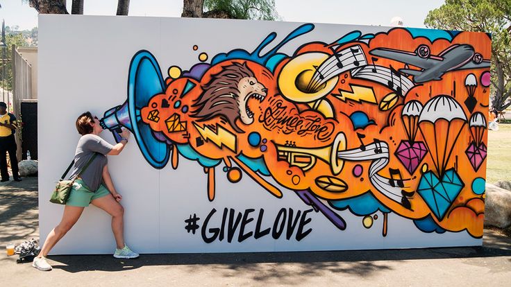 a woman standing in front of a wall with graffiti on it and the words give love painted on it