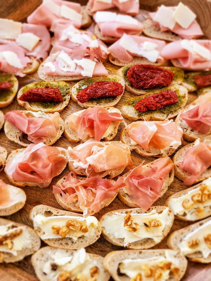 an assortment of appetizers are arranged on a wooden platter with meats and cheese