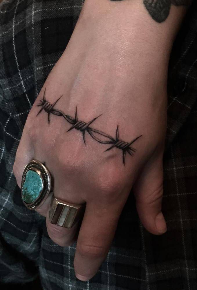 a person's hand with barbed wire tattooed on the ring and an aqua stone