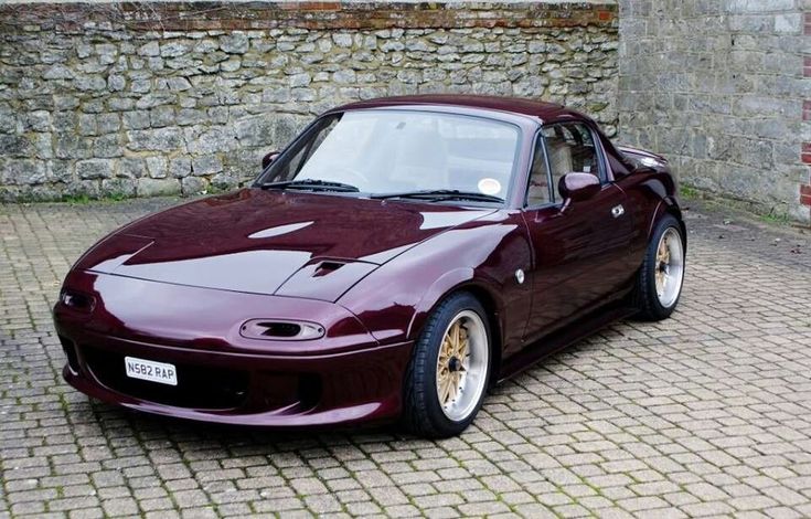 a maroon sports car parked in front of a brick wall on a cobblestone street