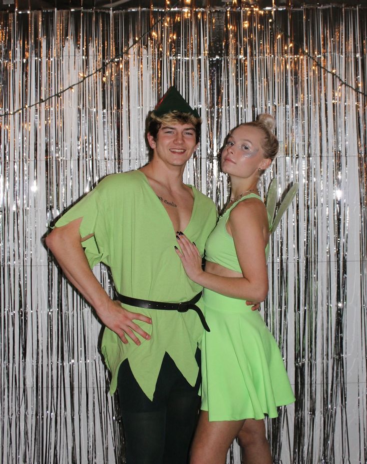 two people dressed up in costumes posing for a photo with tinsel on the wall behind them