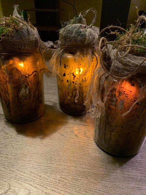 three jars filled with moss and lit candles