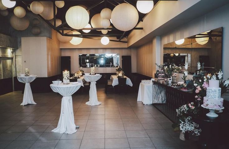 a banquet hall with tables and chairs covered in white linens, decorated with paper lanterns