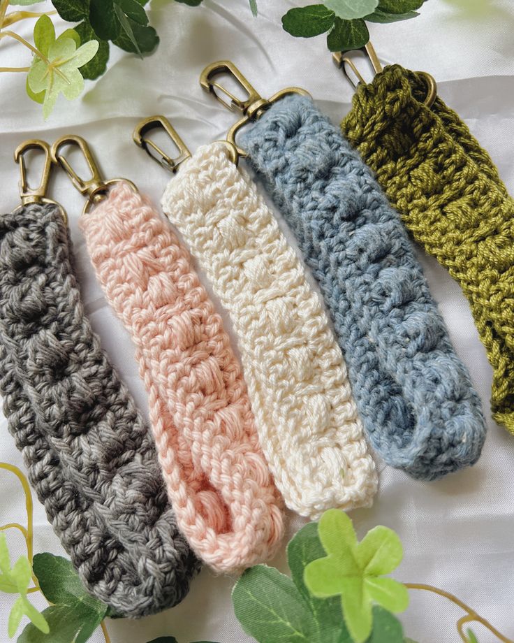 four crocheted key fobs are lined up on a white sheet with green leaves