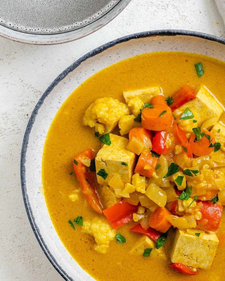 a bowl of soup with tofu, carrots and cauliflower