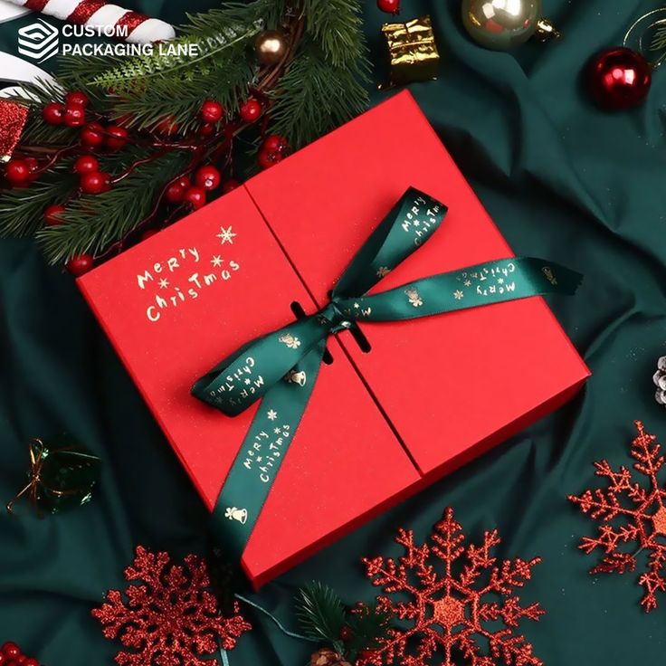 a red gift box with a green ribbon sitting on top of a table covered in christmas decorations