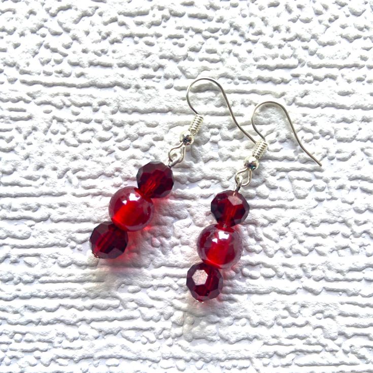 These charming drop earrings each have a central 10mm (0.4in) shiny round bright red glass bead surrounded by two 8mm (0.3in) ruby red faceted acrylic beads.   The beads dangle from silver-plated ear wires with small silicone stoppers to hold them securely in the ear.  The total length of the earrings is 4.5cm (1.8in).   Earrings will be sent to you in a lovely 3.2 x 2in (8 x 5cm) silver gift box.  The price includes UK postage. International postage is reduced accordingly.  Gifts can be sent directly to the recipient. Just choose the gift option at check out. Bead Drop Earrings, Handmade Dangle Earrings, Ribbon Decorations, Silver Gift Box, Earrings Handmade Dangle, Beaded Drop Earrings, Beaded Dangles, Red Glass, Acrylic Beads