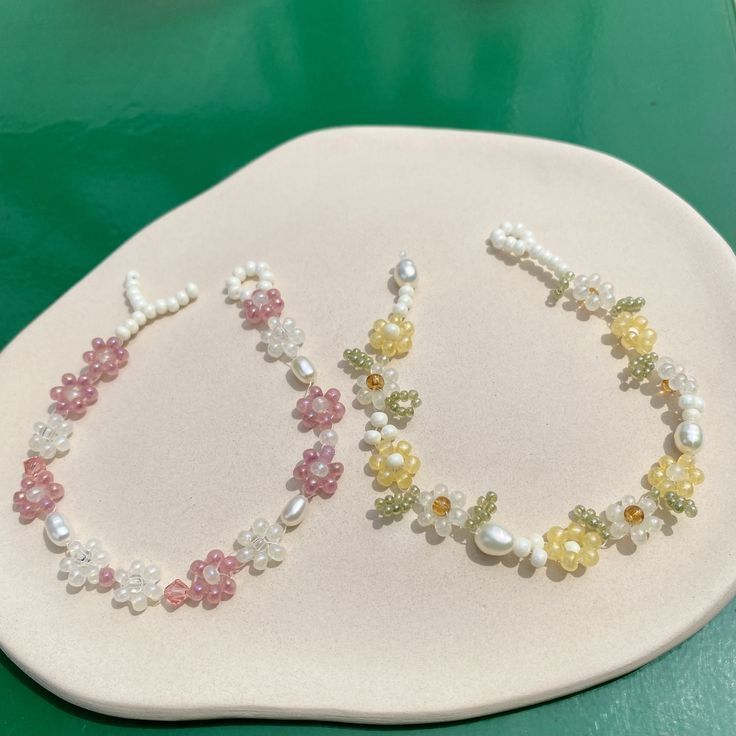 two bracelets made out of pearls and other beads on a white plate next to a green table