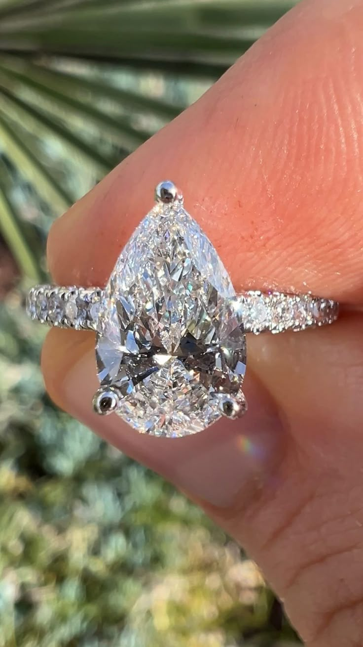 a close up of a person's hand holding a ring with a pear shaped diamond