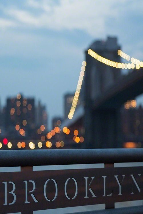 the brooklyn bridge is lit up at night, with lights in the city behind it