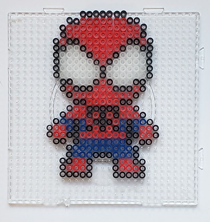 a spiderman made out of legos sitting on top of a white board with black and red beads