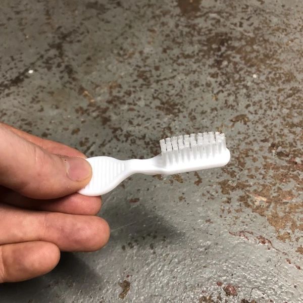 a person holding a white toothbrush in their left hand on a dirty concrete surface