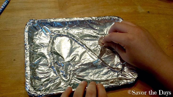 a person is making something out of aluminum foil on a table with a blue pencil