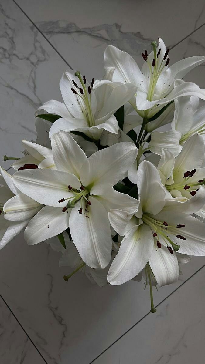 a bouquet of white flowers sitting on top of a marble floored wall next to a vase filled with water