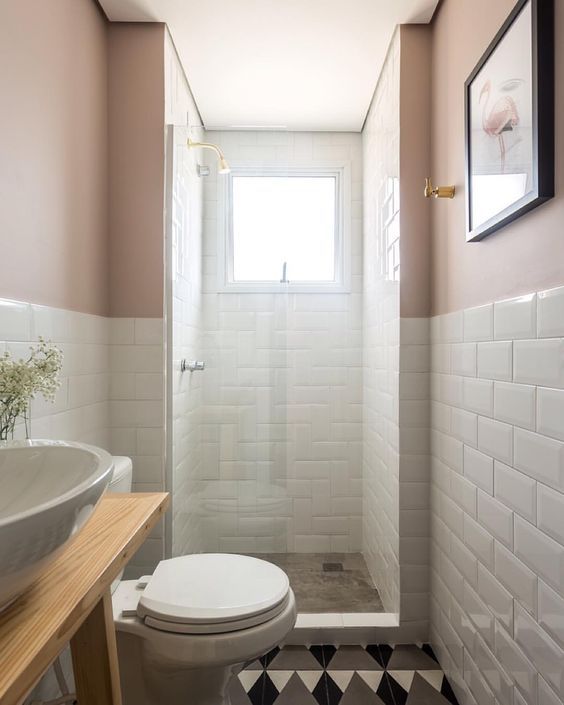 a white toilet sitting next to a sink in a bathroom under a window on top of a tiled floor