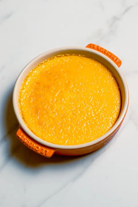 a white bowl filled with yellow liquid sitting on top of a marble countertop next to an orange marker