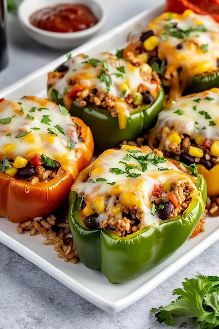 several stuffed peppers on a white plate with rice and garnishes in the background