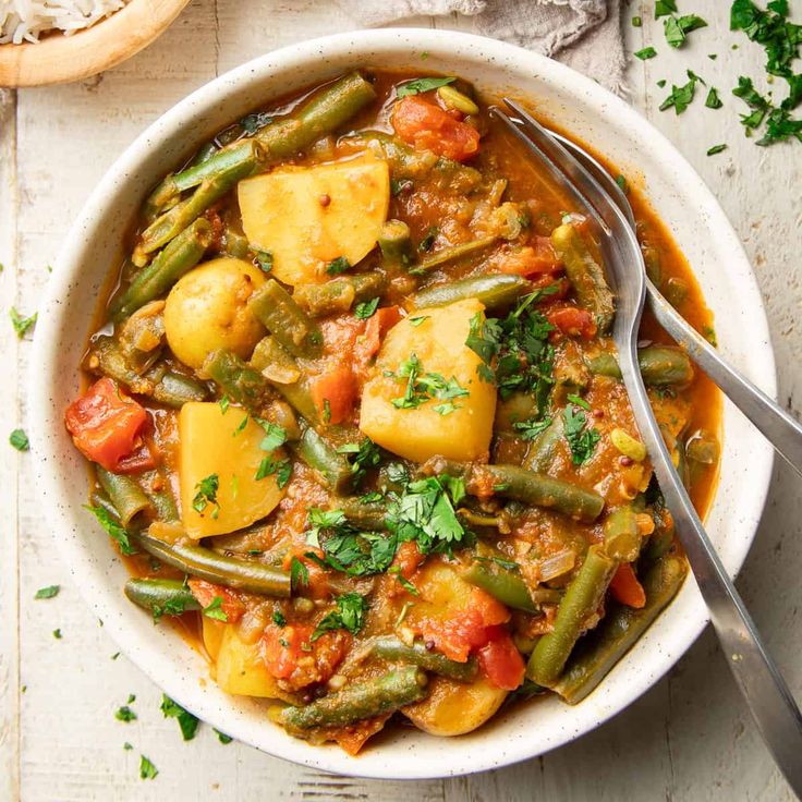 a white bowl filled with stew and potatoes on top of a wooden table next to bread