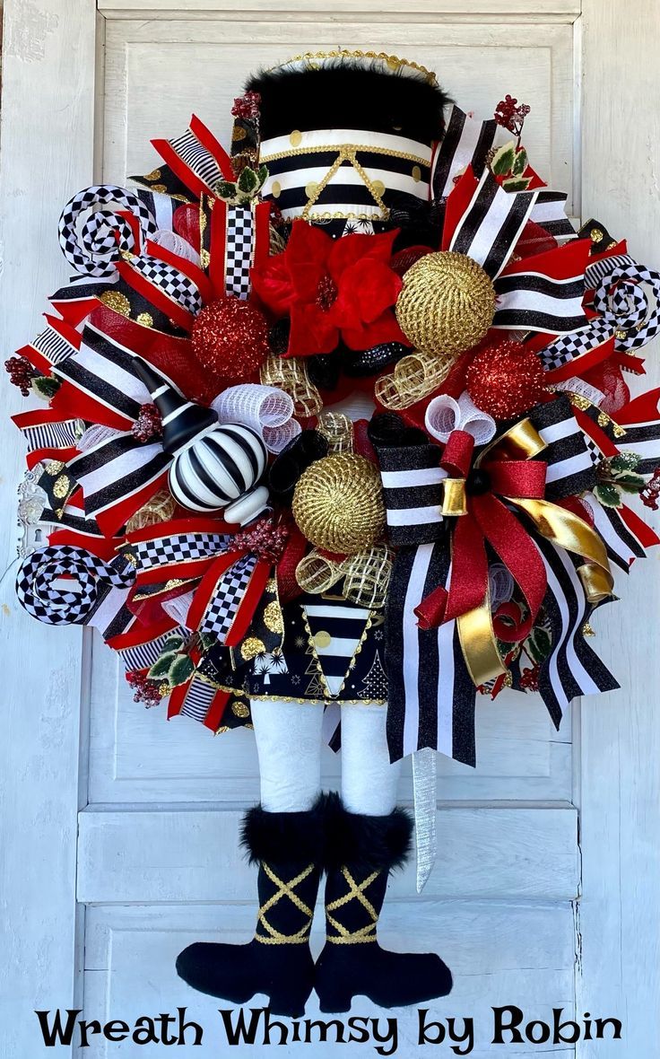 a wreath with red, white and black decorations hanging on the front door for christmas