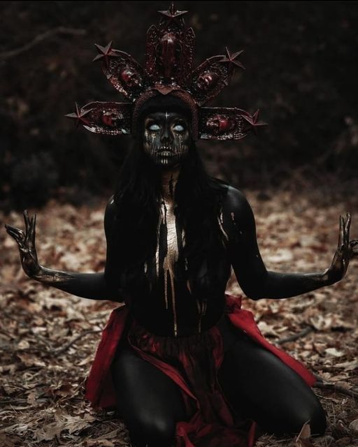 a woman dressed in black and red sitting on the ground with her hands up to her chest