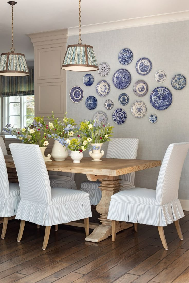 a dining room table with white chairs and blue plates on the wall behind it,