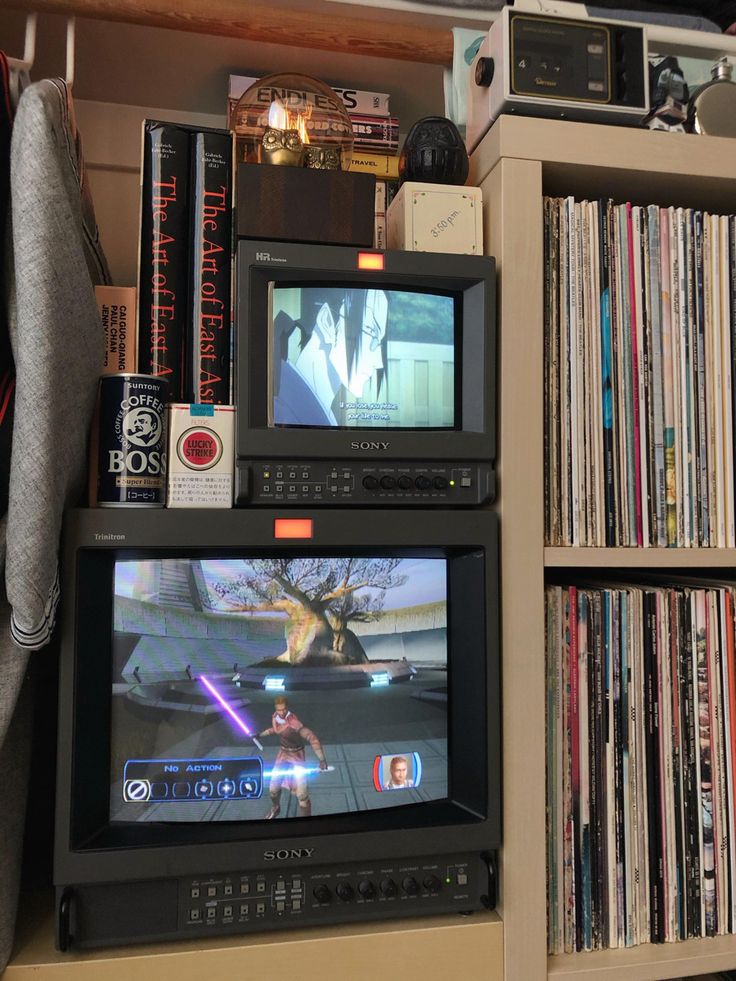 two televisions sitting on top of a shelf next to a bookcase filled with books